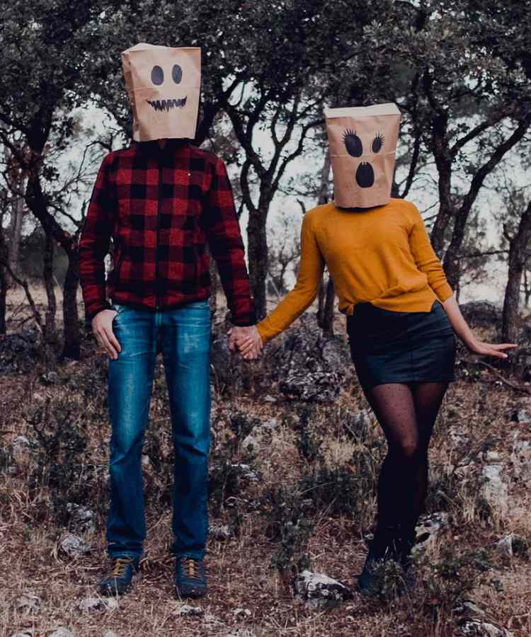 Fantasia de casal para o Halloween: Saco de papel com caras assustadoras. Ele usa camisa vermelha xadrez com preto e calça jeans. Já ela usa blusa laranja, saia preta e meia calça.