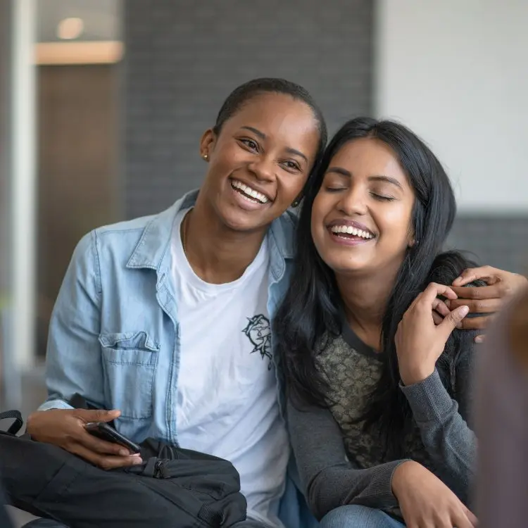 Duas mulheres de pele negra abraçadas sorrindo