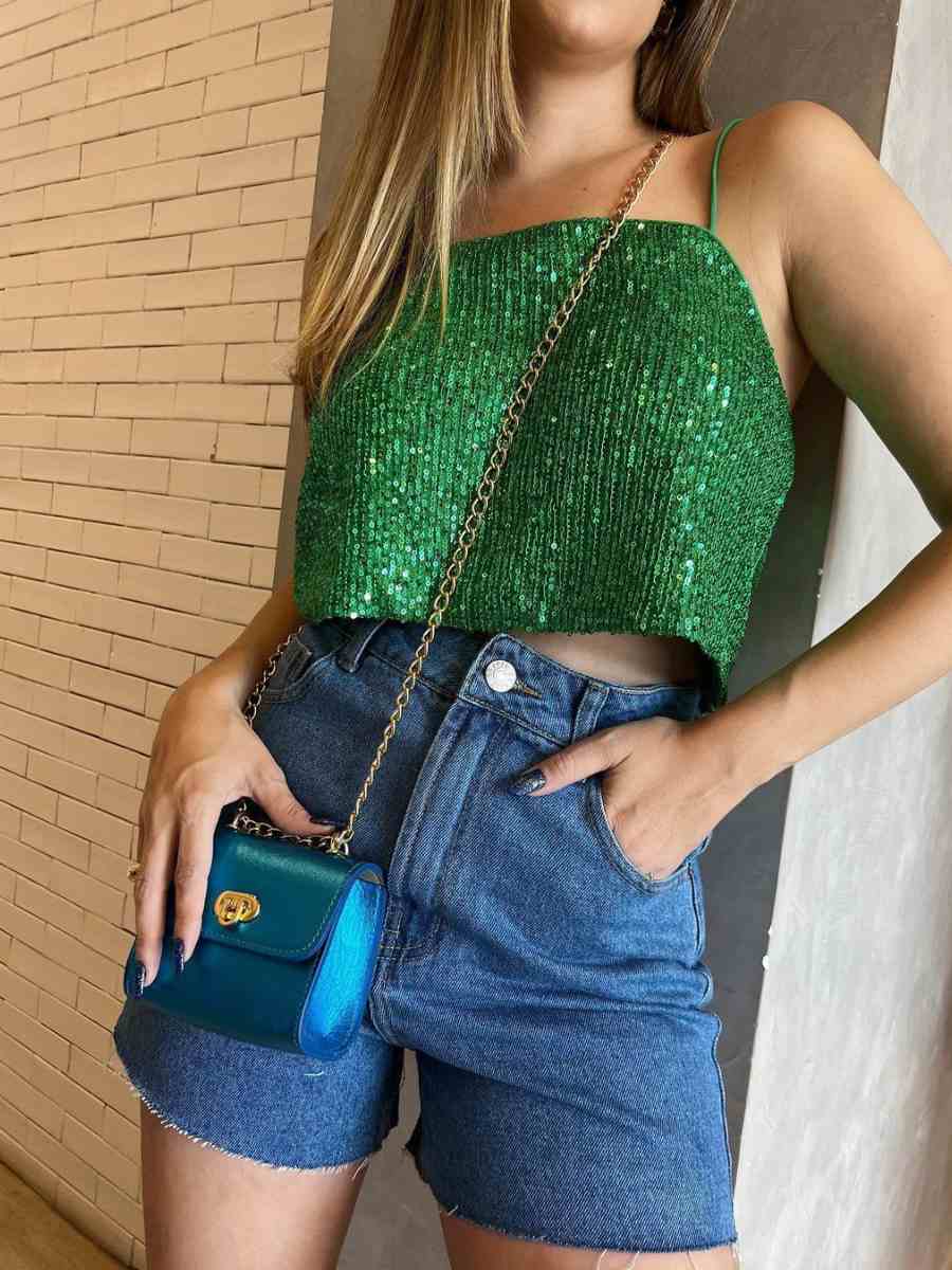 Foto de mulher usando cropped de paetês verde + short jeans + bolsa azul.