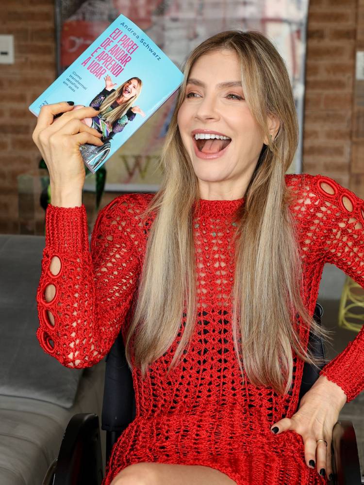 Dea Schwarz de vestido vermelho segurando seu livro "Eu Parei de Andar e Aprendi a Voar"