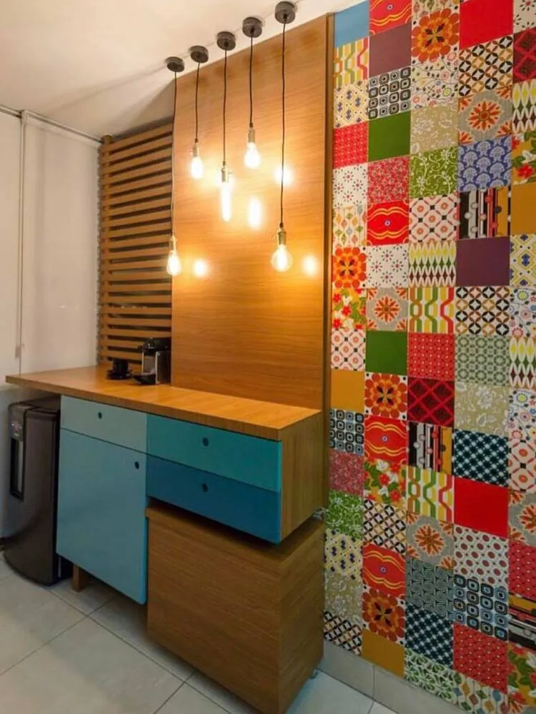 Cantinho do café com móvel de madeira com frigobar, gavetas em diversos tons de azul, luminárias pendulares e parede de azulejos distintos,