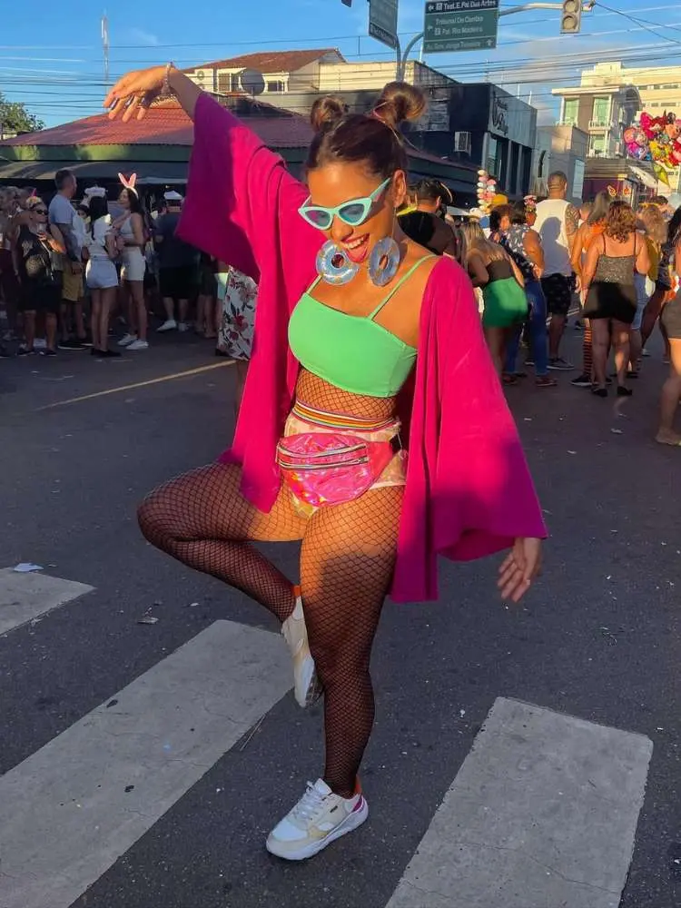 Mulher de pele clara usando top verde, hot pant dourada, pochete e kimono rosas 
