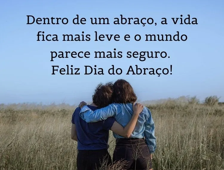 Foto de duas pessoas de costas se abraçando no campo e frase: Dentro de um abraço, a vida fica mais leve e o mundo parece mais seguro. Feliz Dia do Abraço!