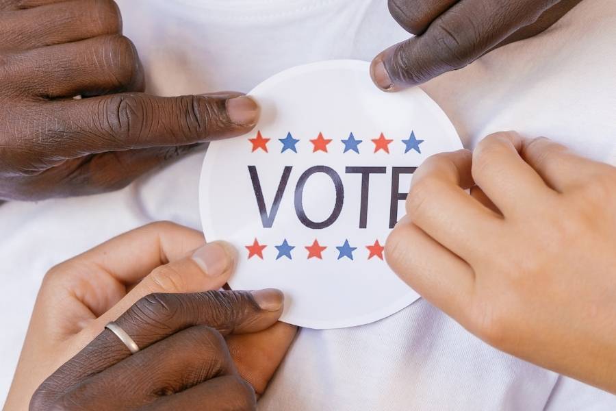Mãos colocando um broche escrito "Vote" em uma camiseta branca. 