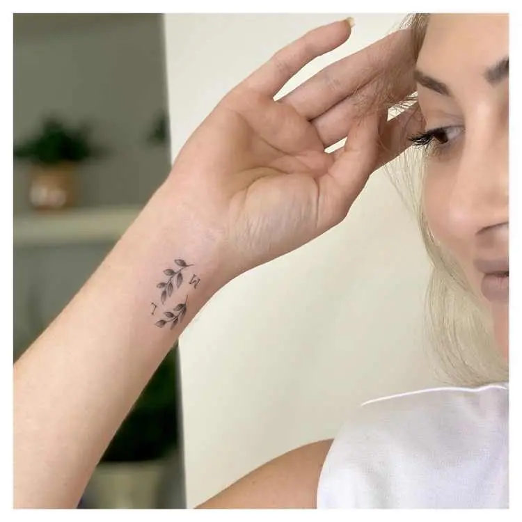 Mulher loira de pele clara com tatuagem de ramos pequenos e letra M no pulso