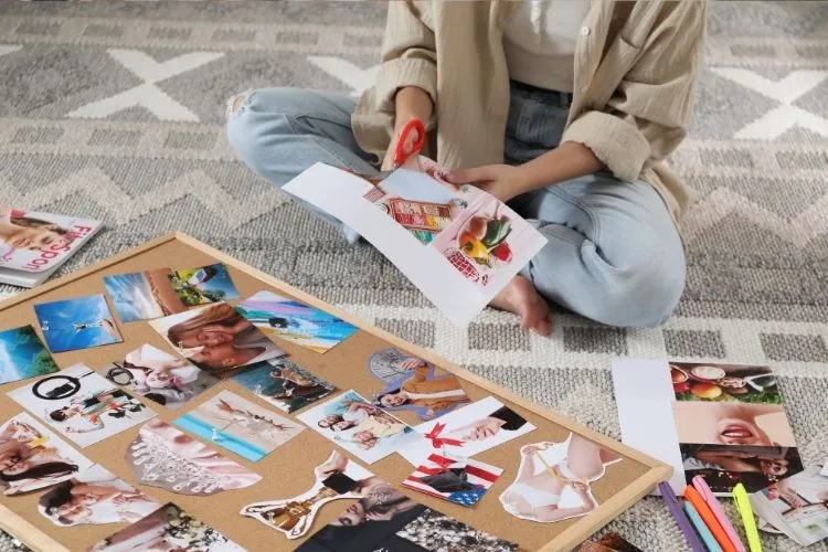 Mulher sentada no chão recortando imagem para colar em seu vision board
