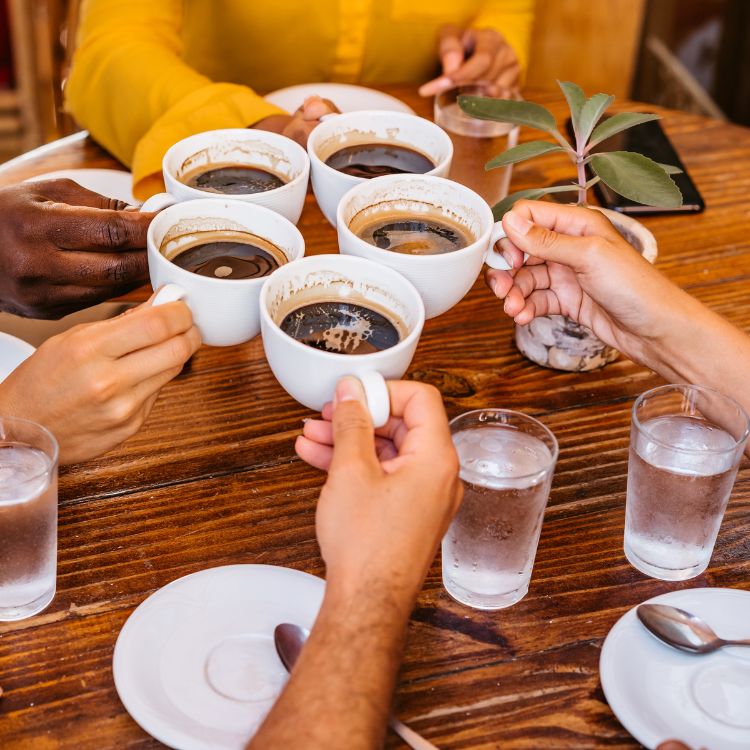 Pessoas sentadas à mesa, brindando com xícaras de café