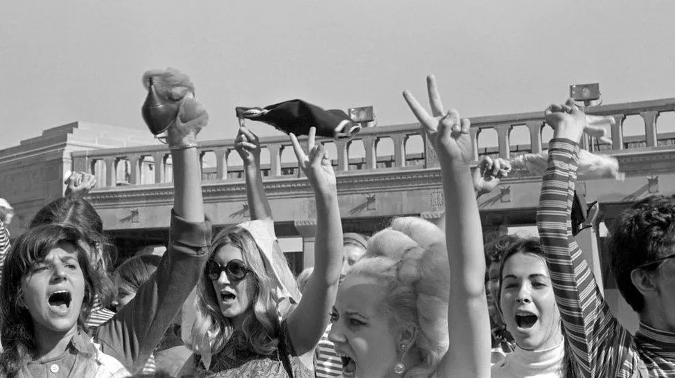 Foto em preto e branco do protesto de mulheres em 1968 contra o concurso Miss America em Nova Jersey conhecido pela queima de sutiãs Protesto de mulheres em 1968 contra o concurso Miss America em Nova Jersey, acerca da moda e cidadania feminina.