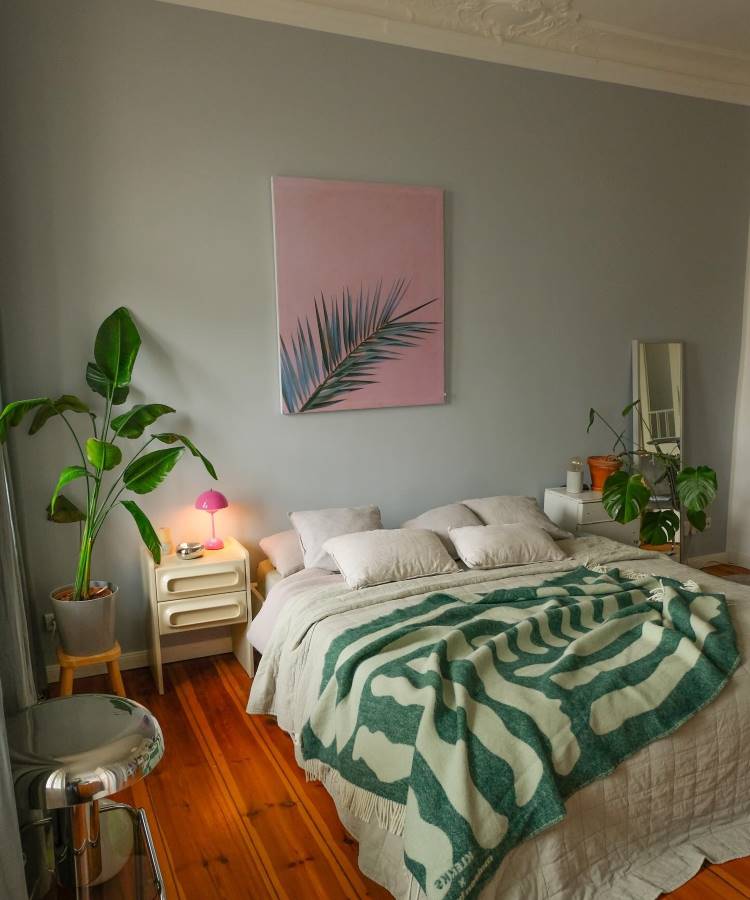 Quarto com decoração Feng Shui, apresenta cama centralizada com colcha verde, plantas em vasos promovendo energia vital, luz natural abundante, paleta de cores suaves e detalhes harmoniosos. Quadros simples e móveis minimalistas completam o ambiente equilibrado e acolhedor.
