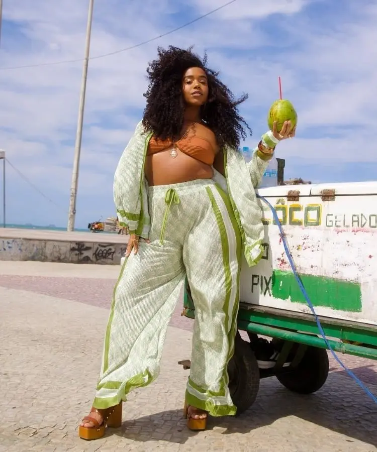Foto de Mari Lobo, uma das influenciadoras negras de moda, usando biquíni marrom e conjunto de calça e camisa branco e verde