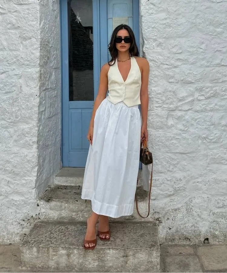 Foto de mulher morena usando colete e saia mídi brancos, um dos looks para trabalhar no calor