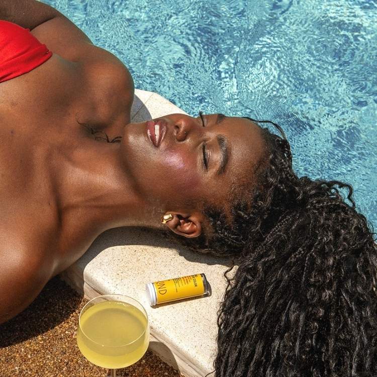 Mulher negra de olhos fechados tomando sol na beira da piscina