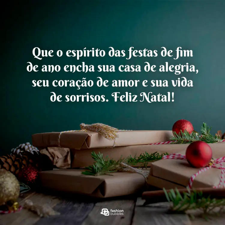 Foto de mesa com presentes, bola de natal, pinha e frase "Que o espírito das festas de fim de ano encha sua casa de alegria, seu coração de amor e sua vida de sorrisos. Feliz Natal!"