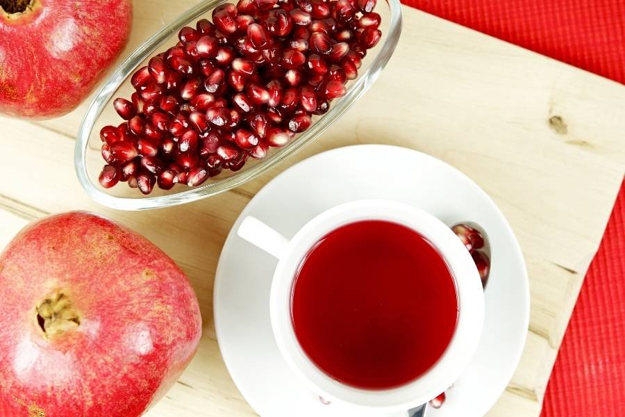 Xícara com chá de romã com duas frutas ao lado.