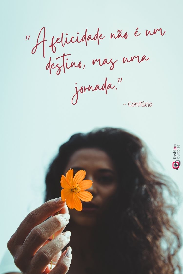 A imagem apresenta uma citação inspiradora de Confúcio: "A felicidade não é um destino, mas uma jornada". No plano inferior, uma pessoa segura delicadamente uma flor cosmos laranja vibrante, com o rosto levemente desfocado ao fundo. A cena sugere reflexão e apreciação da beleza nos pequenos detalhes da vida.







