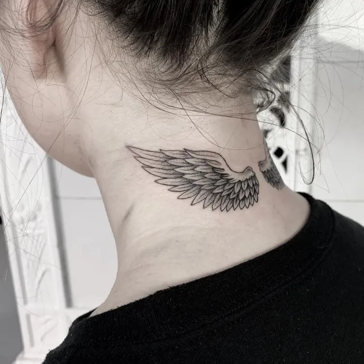 A imagem mostra uma pessoa de costas com cabelo preso. Ela tem uma tatuagem no pescoço de asas de anjo estendendo-se horizontalmente, detalhadas em preto. A tatuagem está localizada na base do pescoço, logo abaixo da linha do cabelo, e é feita com traços finos e delicados.




