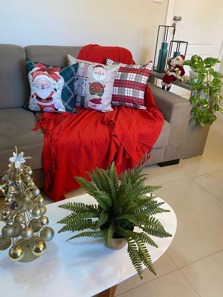 Sala de estar decorada co, almofadas natalinas, mini árvores de Natal e manta vermelha.