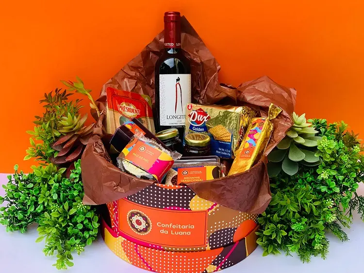 caixa de papel colorida com itens para presente de natal como vinho e guloseimas 