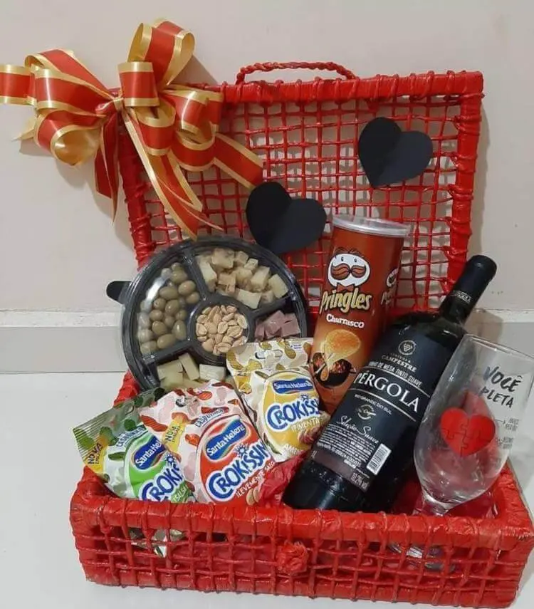 Cesta vermelha com petiscos, batata chips, vinho, taça, laços e corações