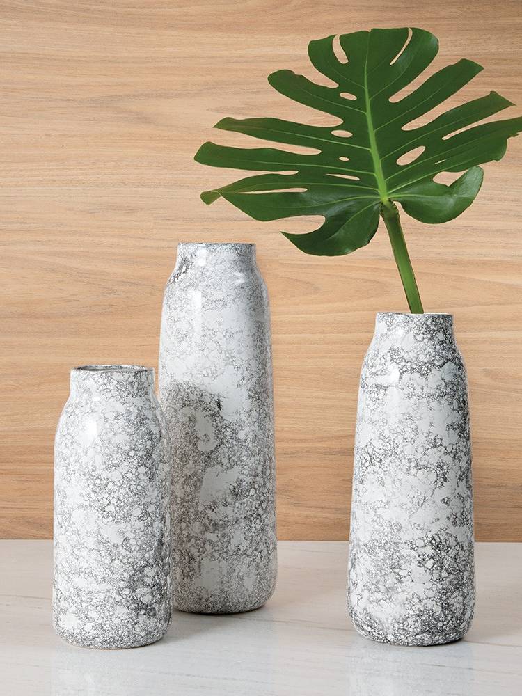 3 vasos minimalistas marmorizados. Um deles, o da direita, contém uma folha de costela-de-adão. 