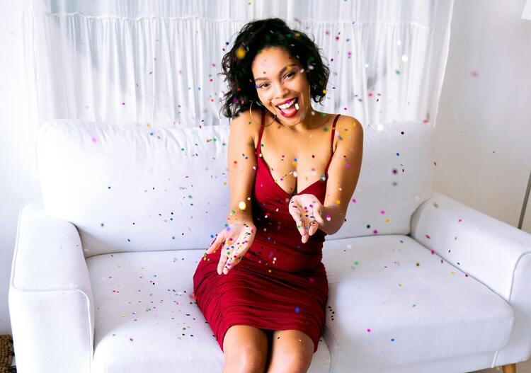 Mulher com vestido vermelho sentada em um sofá branco e confetes ao seu redor