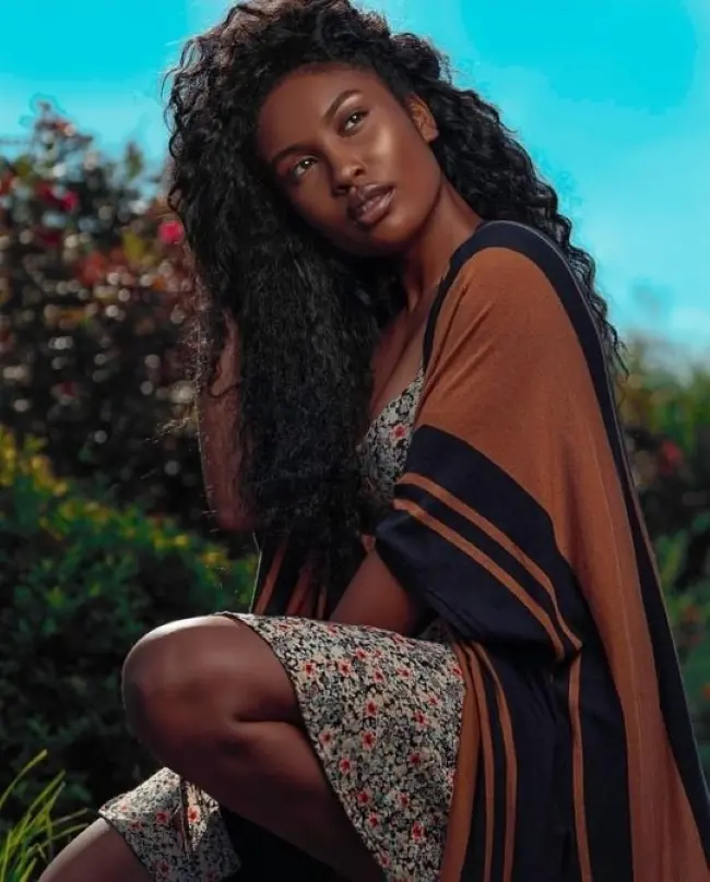 Frase para foto pensativa mulher negra com cabelos crespos e longos usa vestido floral e kimono marrom e preto Frase para foto pensativa mulher negra