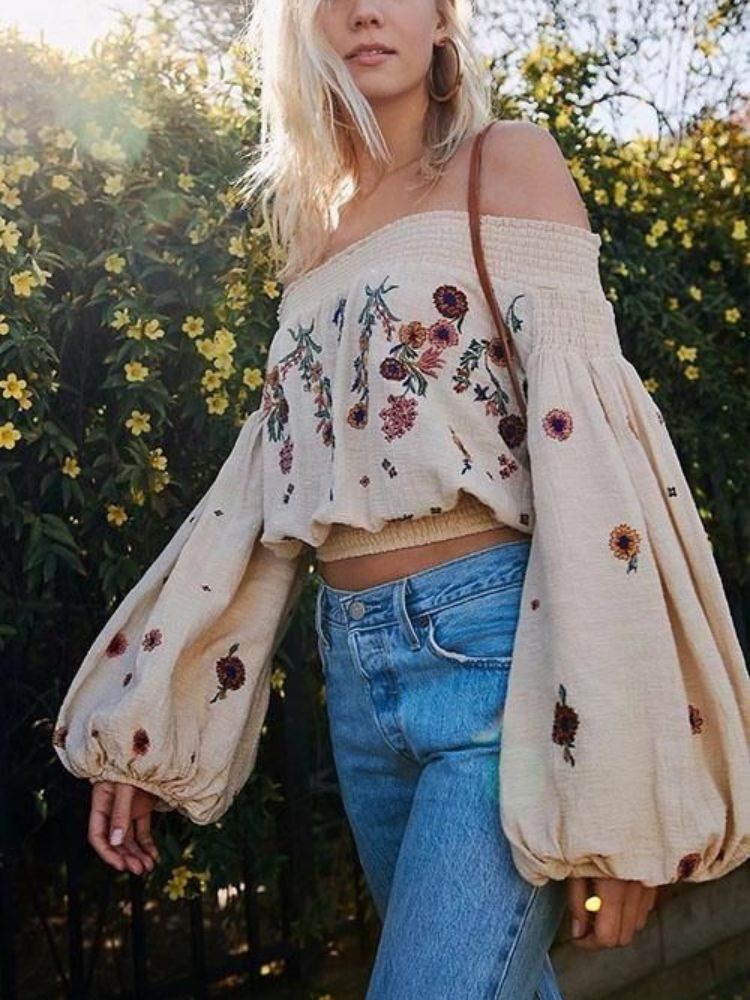 Mulher de pele clara com blusa bufante com estampa de flores e calça jeans. 