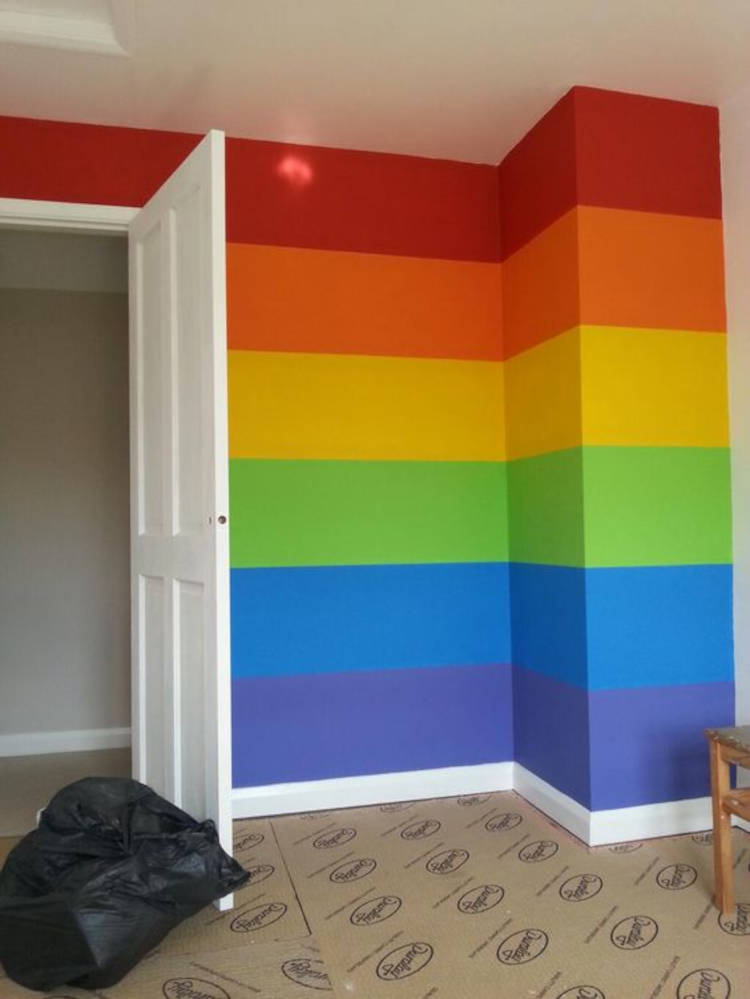 Parede com as cores da bandeira LGBTQIA+, chão forrado de papelão e porta aberta branca