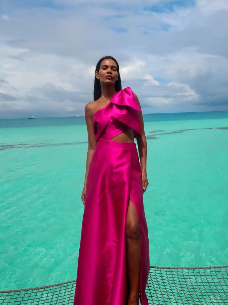 Mulher de pele morena no mar usando vestido rosa cut out com maxi laço no ombro 