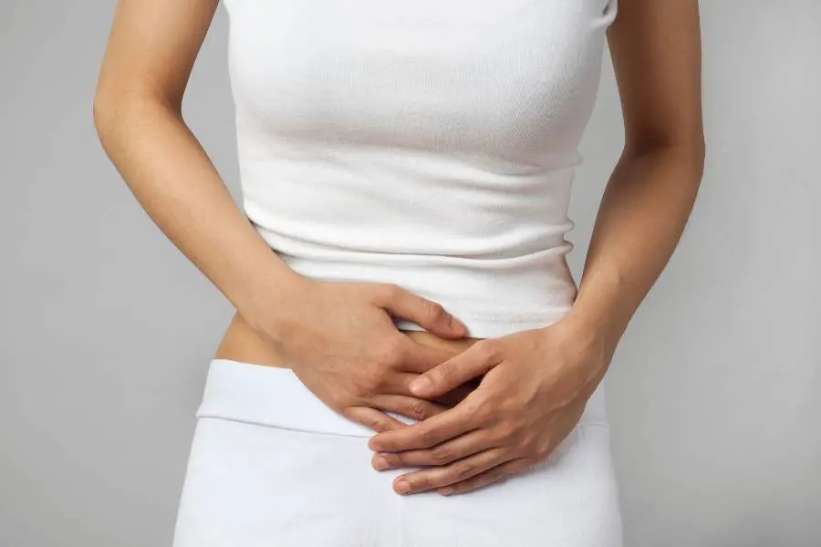 Mulher com roupa branca e mãos indicando cólica menstrual.