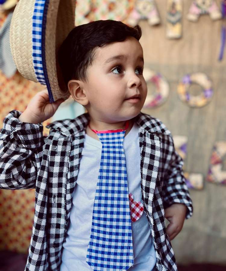 Menino usando camisa xadrez preta e branca, gravata xadrez azul e chapéu de palha.

