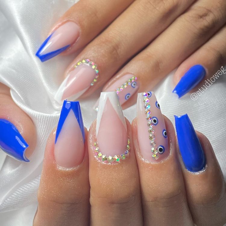 Unhas decoradas em tons de azul com pedraria e olho grego