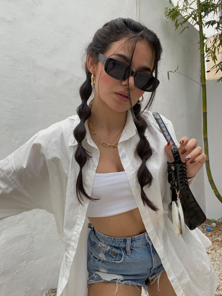 Mulher de pele clara de top branco, camisa branca, shorts jeans, acessórios e dupla bubbles braids