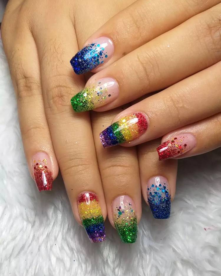 Mão com unhas decoradas coloridas: Polegar: não aparece na foto Indicador: glitter azul mesclado Médio: glitter verde mesclado Anelar: arco-íris de glitter Mínimo glitter vermelho mesclado
