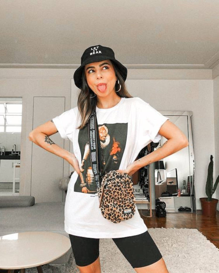 Mulher de pele clara com biker shorts preto, shoulder bag de onça e camiseta branca em looks para o Lollapalooza