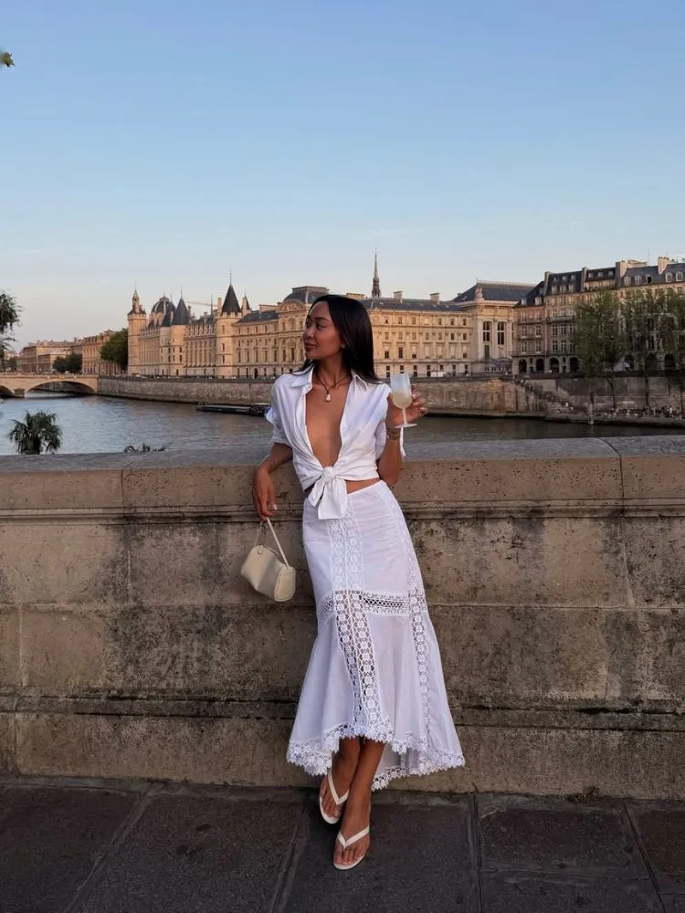 Mulher de origem asiática usando camisa branca de amarração e saia midi branca com renda