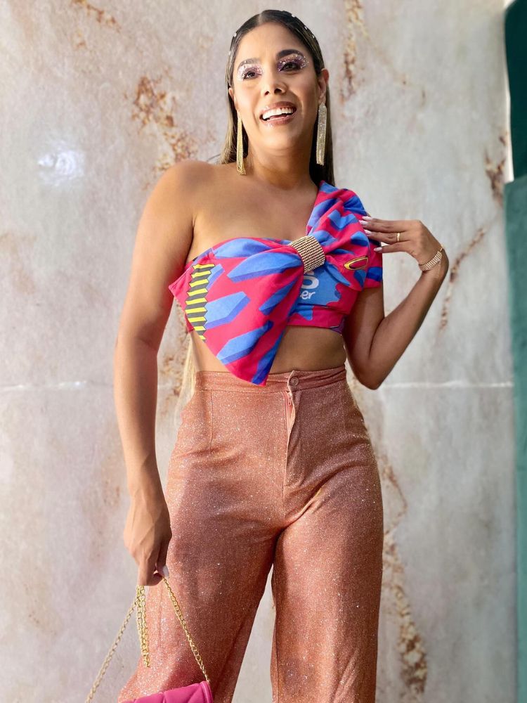 Mulher de pele clara com abadá azul e rosa customizado em top com laço maximalista e calça bege