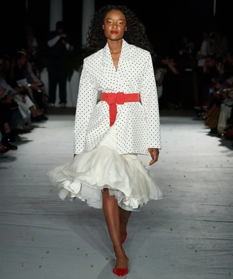 Foto de modelo na passarela usando blazer de bolinhas com saia branca rodada