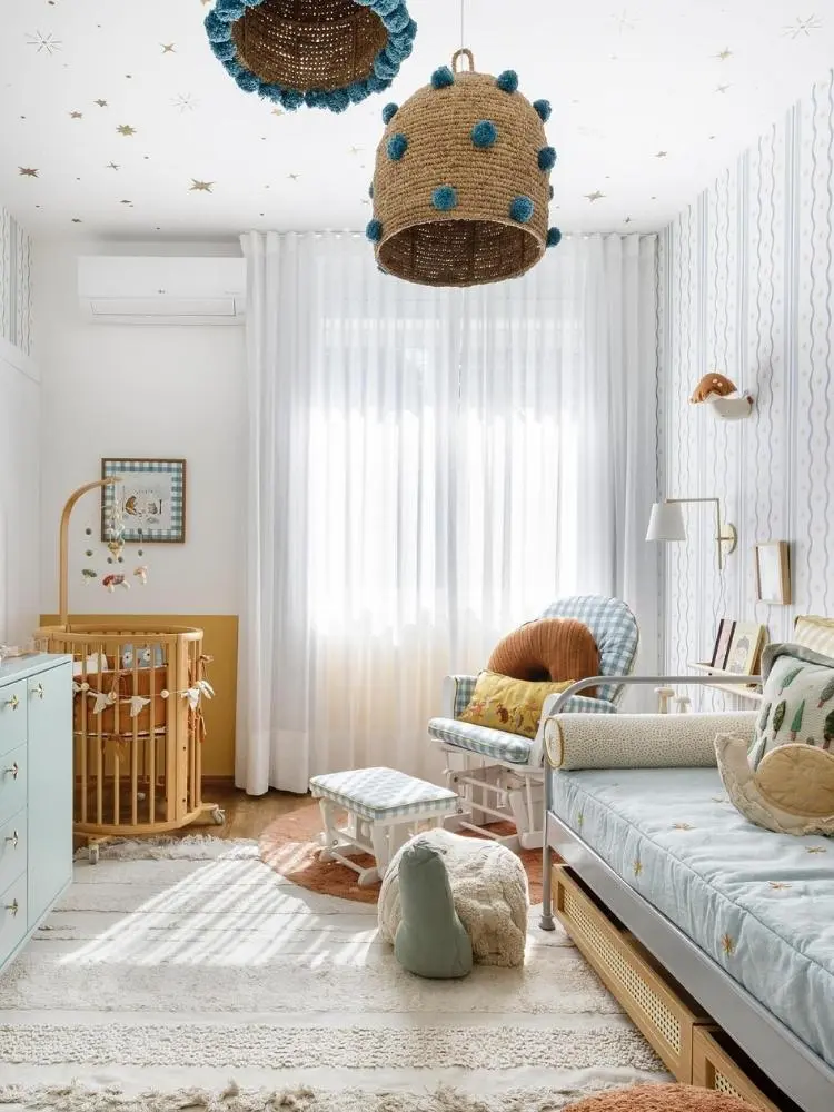 Quarto de bebê em tons claros com lustres artesanais, berço, cama, tapete e brinquedos 