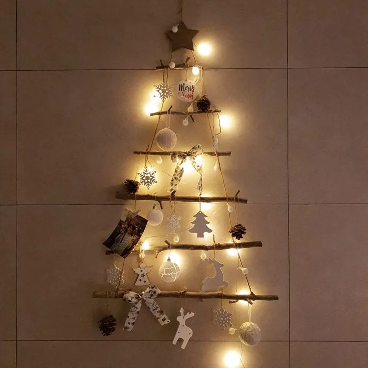 Parede de azulejo bege com pequena árvore-de-natal de galhos, com enfeites natalinos branco e dourado e pisca-pisca