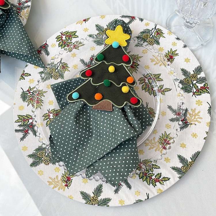 Sousplat de ramos natalinos com prato transparente e guardanapo verde com árvore de Natal. 