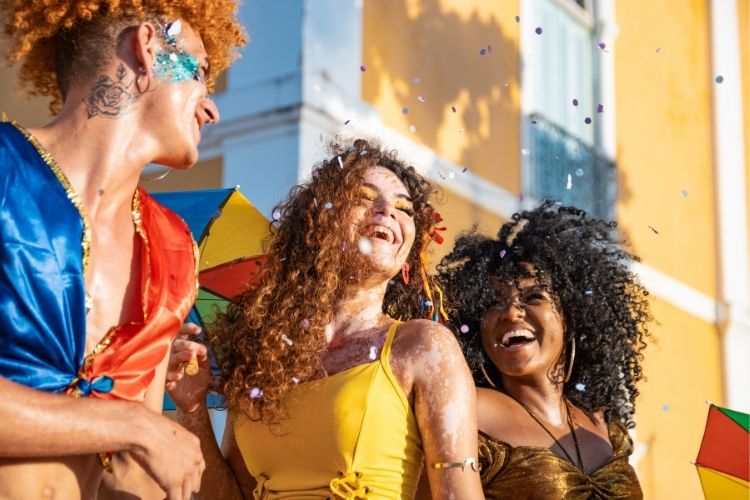 Homem ruivo de pele clara, mulher de pele clara e cabelo castanho e mulher de pele negra e cabelo preto curtindo o Carnaval. 