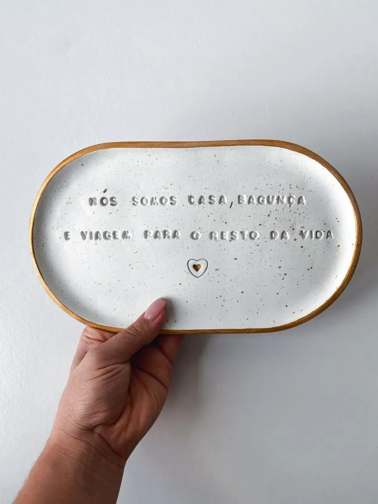 Mão segurando bandeja branca com coração e frase: nós somos casa, bagunça e viagem para o resto da vida  