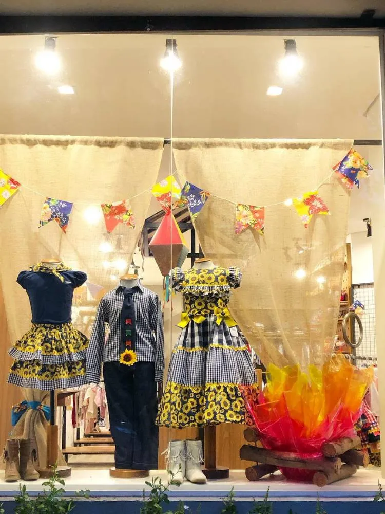 Vitrine com manequins de festa junina, bandeirinhas e fogueira de papel celofane 