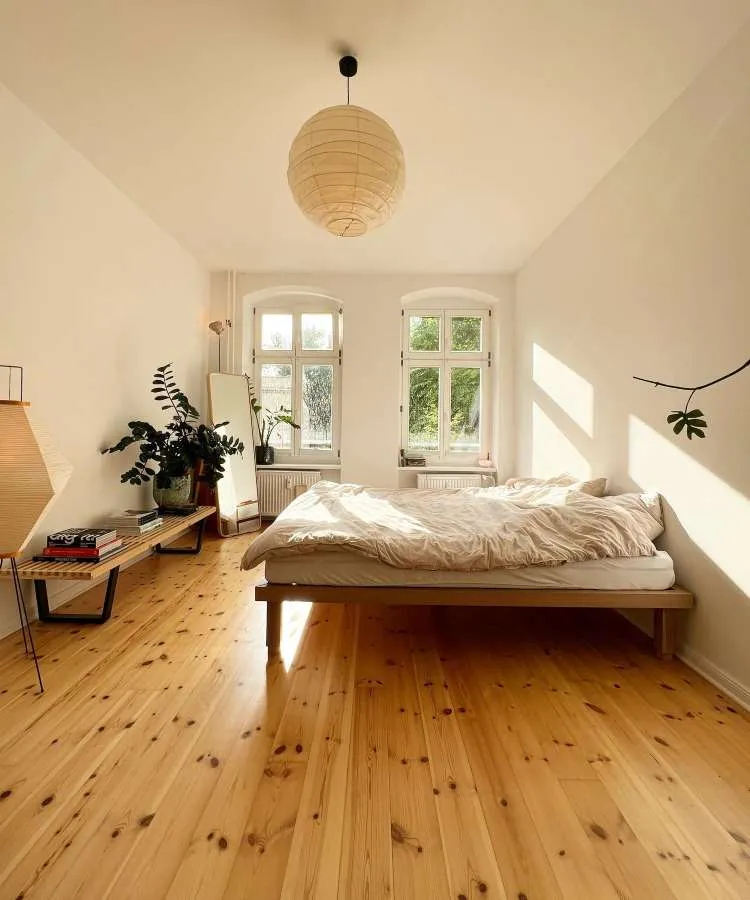 Quarto de casal com espelho retangular  no canto da parede, de frente para janela. Cores predominantes: palha, madeira, off-white, branco
