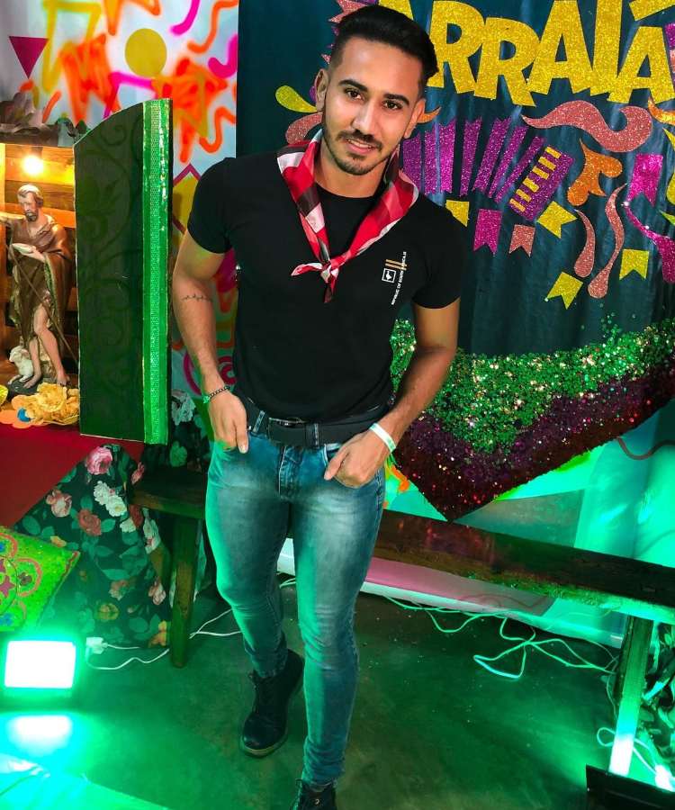 Homem com look junino, camiseta preta, calça jeans e lenço xadrez vermelho no pescoço