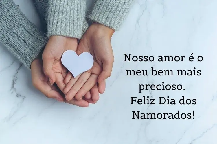 Foto de duas pessoas de pele clara usando casaco cinza, com mãos sobrepostas e coração branco, além de frase 'Nosso amor é o meu bem mais precioso. Feliz Dia dos Namorados!"