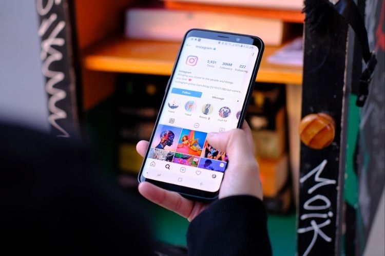 Mão segura um smartphone exibindo a interface do Instagram. A pessoa navega pelo feed de postagens, destacando a exploração de conteúdo. A imagem sugere a interação com mídias sociais no cotidiano.







