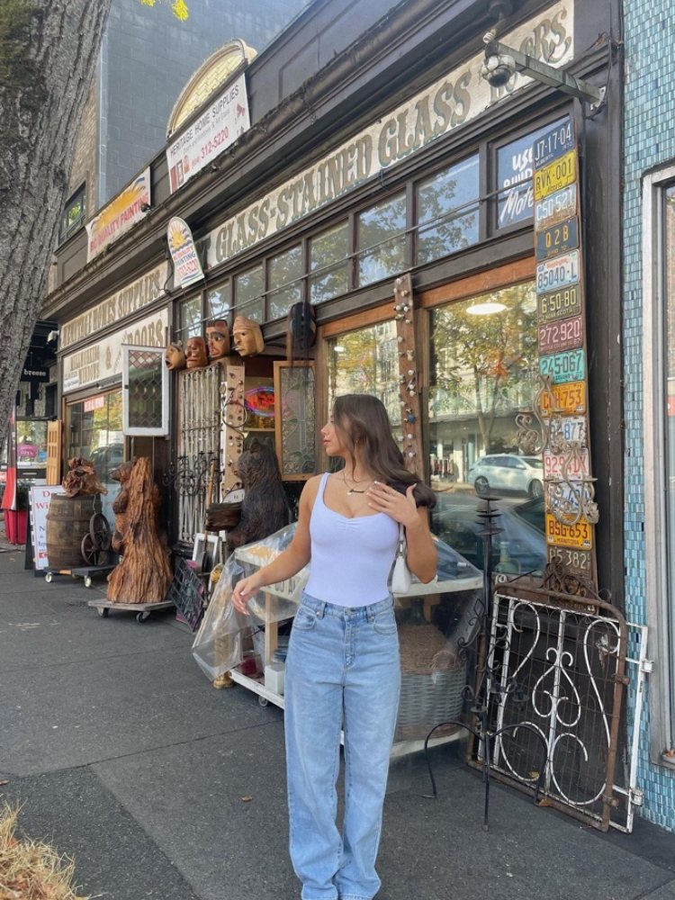 mulher usando regata branca com calça jeans wide leg azul e bolsa branca estilo baguette