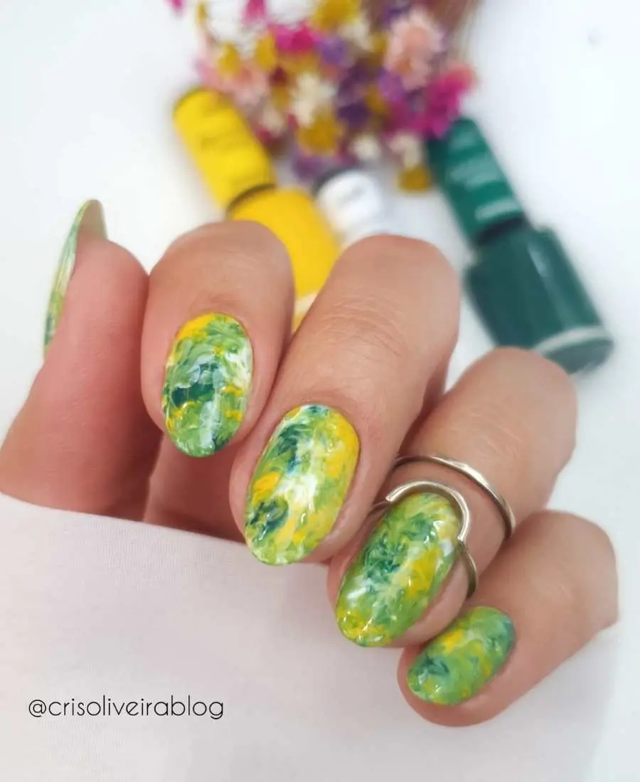 Imagem de mão com unhas decoradas de Brasil.  Cores usadas, verde, amarelo e branco. Cores usadas, verde, amarelo e azul. Efeito mármore com as cores mescladas em todas as unhas.
